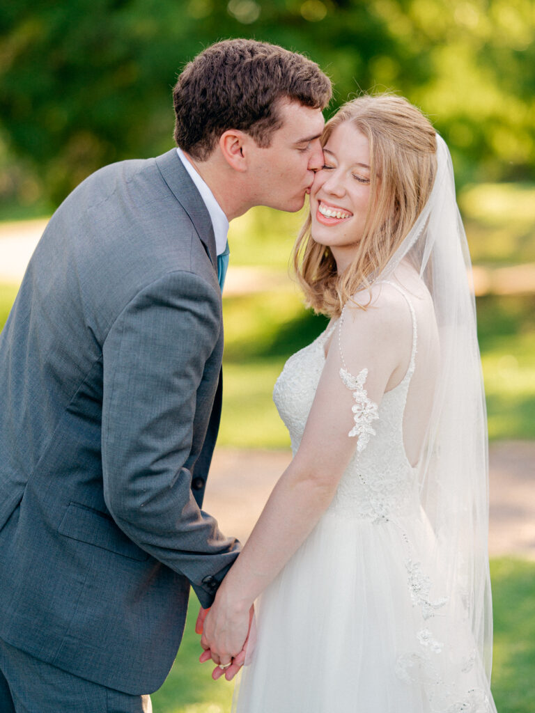 Groom kisses bride on the cheek as she smiles back at the camera during intimate elopement.