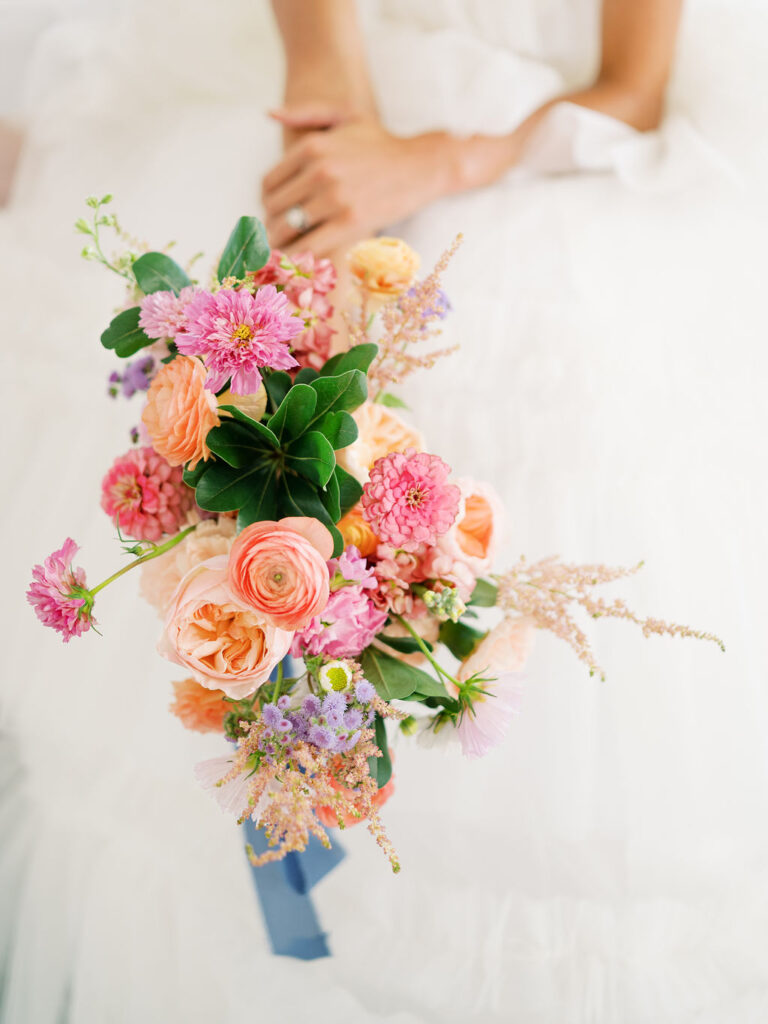 A close up of a bride holding a vibrant pink wedding bouquet with a blue ribbon.