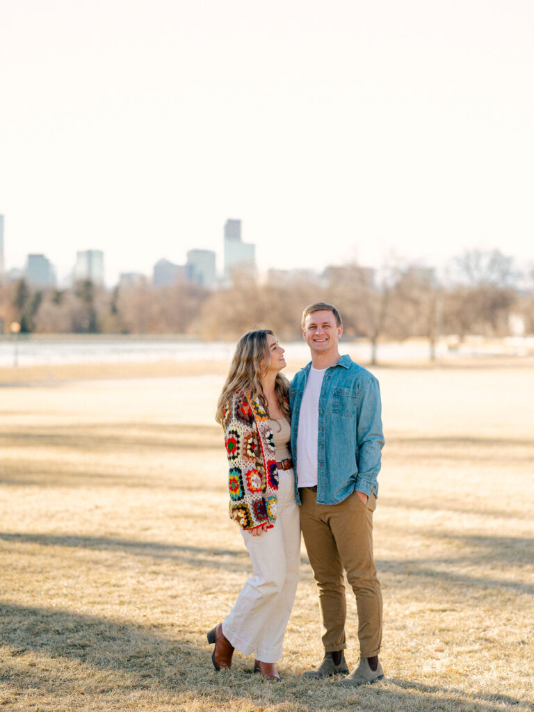 Couple stands side by side in front of the Downtown Denver skyline.