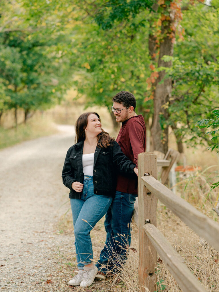 A couple stands on a gravel road surrounded by trees changing color.