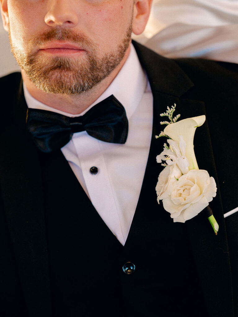 A close up of a groom wearing a tux and a boutonniere of white flowers.