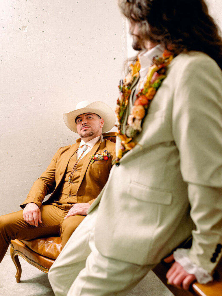 Two grooms sit in a basement speakeasy in Boulder, Colorado at a western inspired LGBTQ wedding.