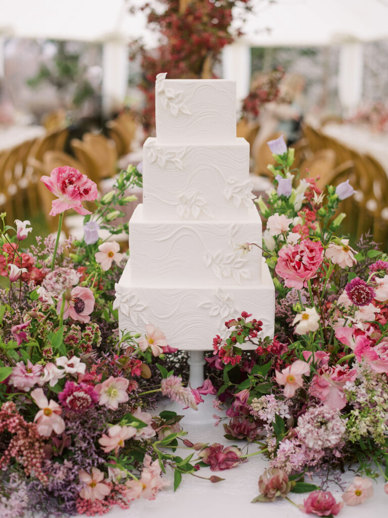 All white wedding cake surrounded by whimsical pink and magenta flowers.