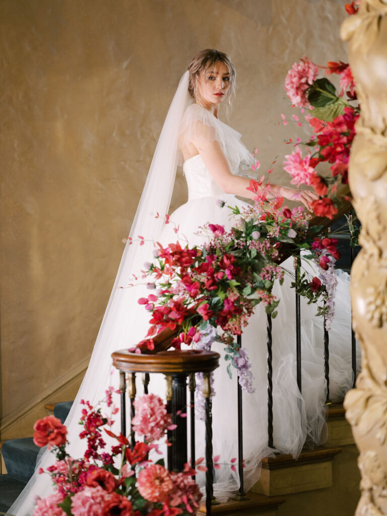 Bride on staircase with magenta floral installation winding up the rail.