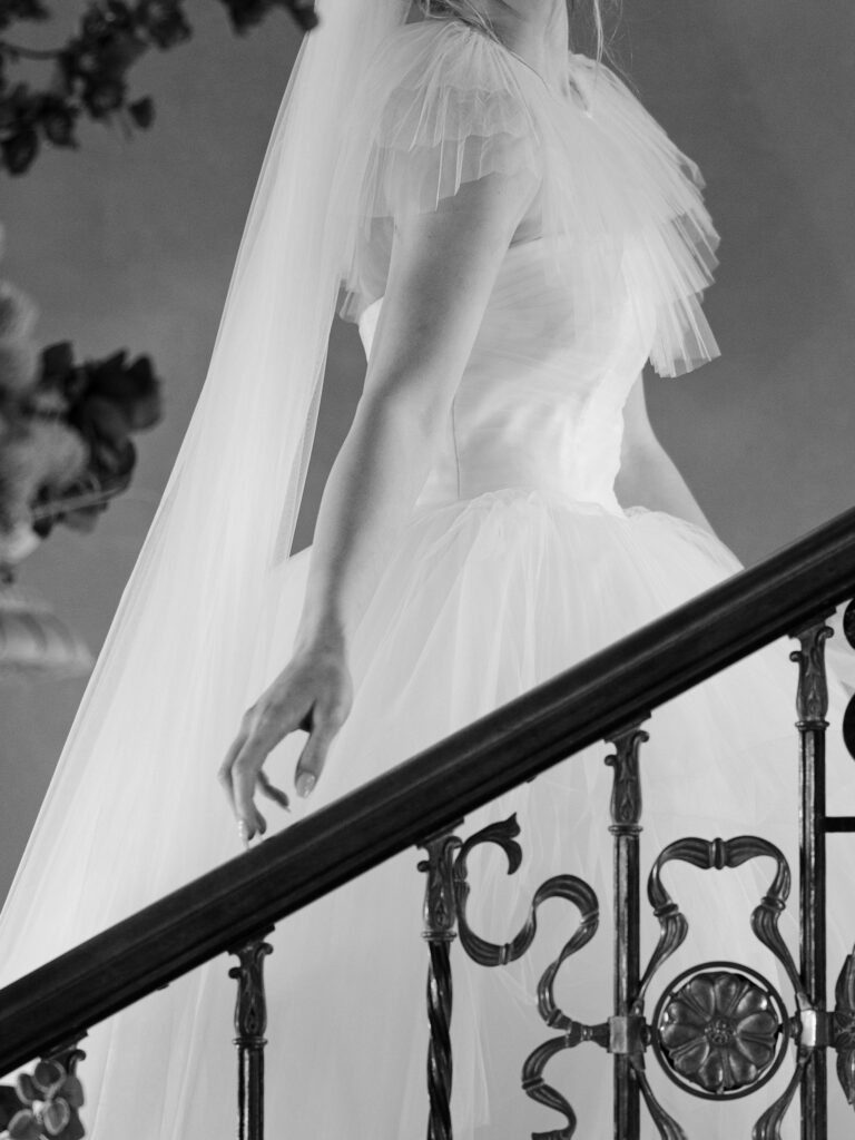 Bride runs her hand up a staircase rail in up close photo of wedding dress.