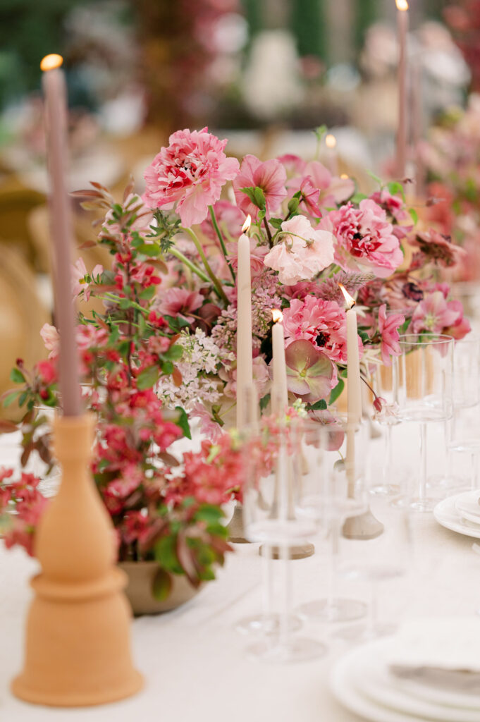 Dinner table at tented wedding reception covered in candles and pink flowers.