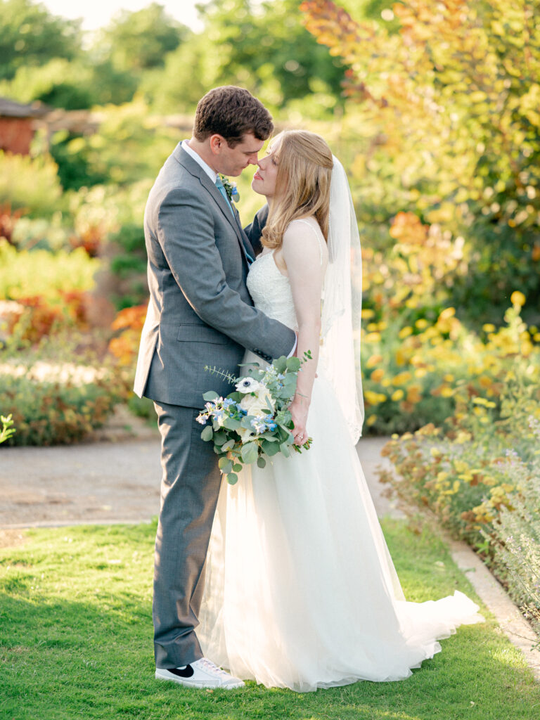 Bride and groom lean in for a kiss in garden during golden hour.