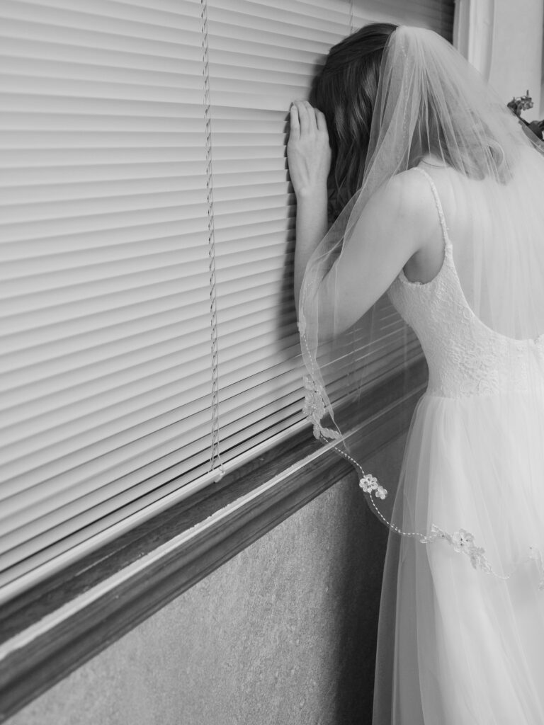 Bride peeks through window during intimate elopement.