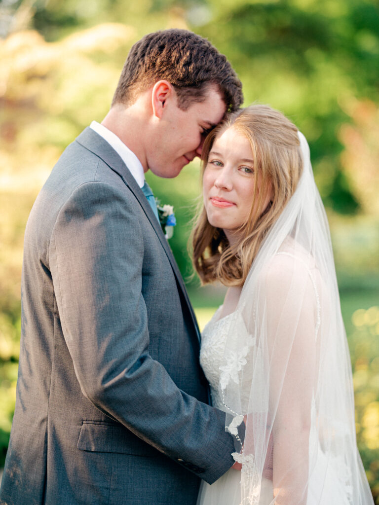 Bride looks at camera as groom holds her close during golden hour portraits at intimate elopement.