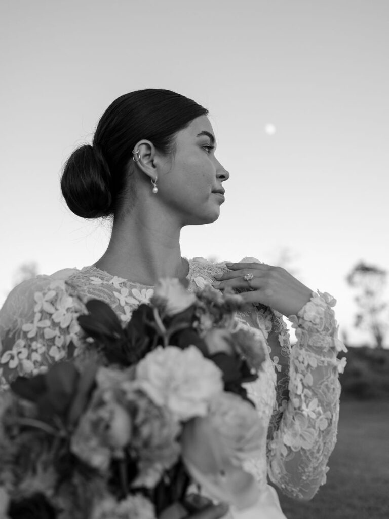 A close up image of a bride looking over her right shoulder, with her hand resting gently on her collarbone.