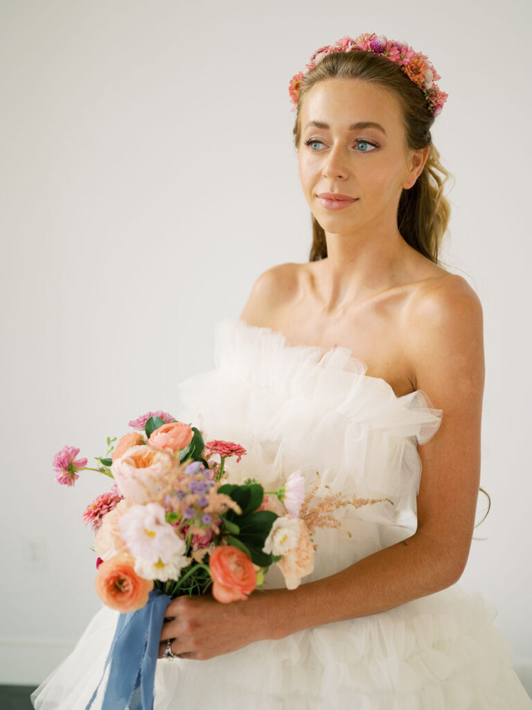 Bride holding bouquet with pink flowers and wearing a floral headband looks off to the left.