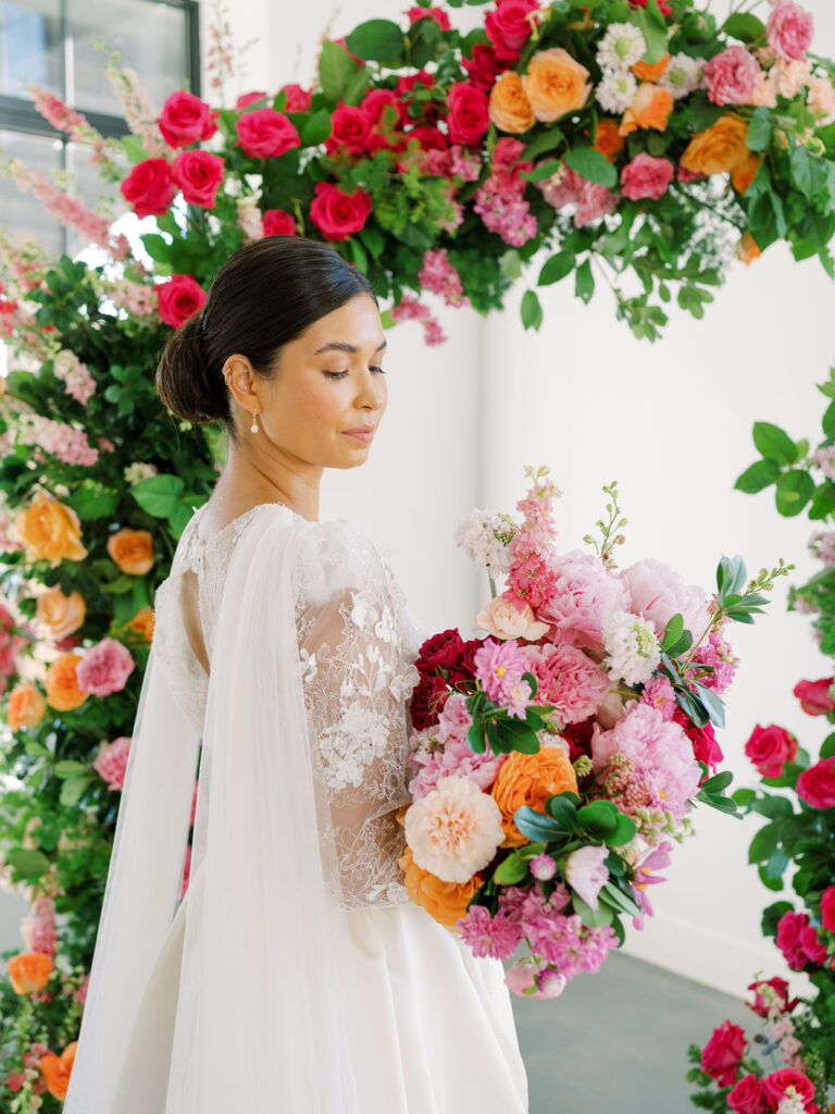 A bride holding a large pink and orange bouquet looks down at her flowers.