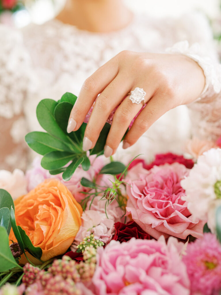 A close up of a bride's engagement ring as she lightly touches the flowers in her bouquet.