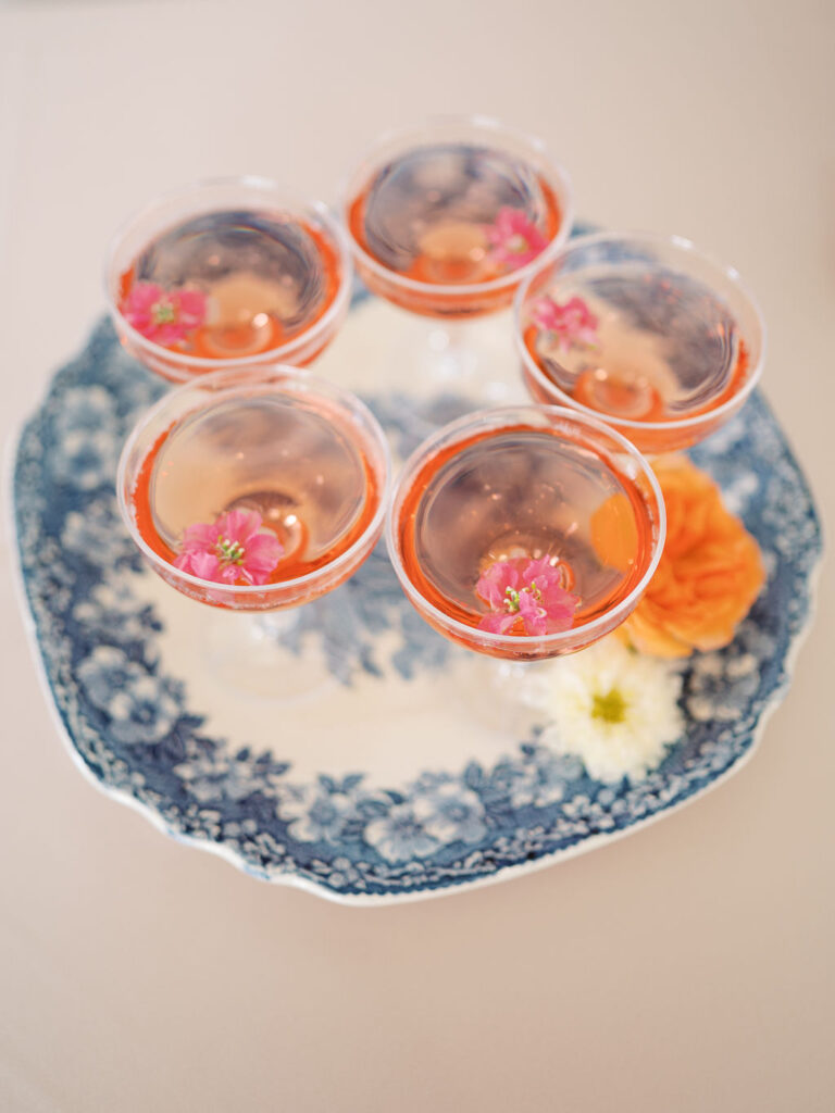 Pink champagne with small flowers in the glasses sits on top of a blue and white floral patterned tray.