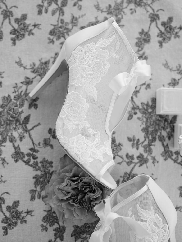Lace bridal heels with a bow on a floral backdrop.