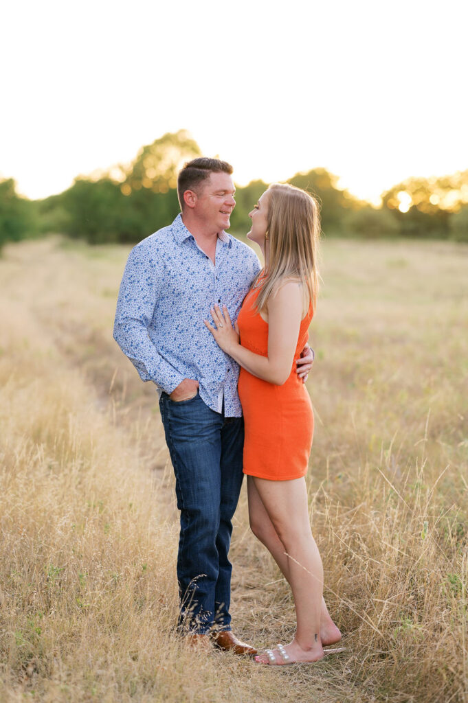 In a field on a ranch, bride and groom look lovingly at each other during engagement session