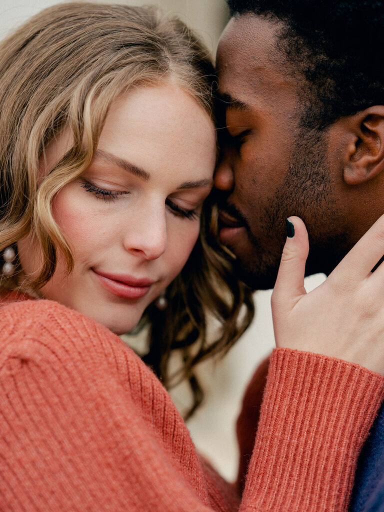 A couple in a tender embrace. On the left, the girl has her face turned toward the camera, but is looking down. On the right, the guy has his eyes closed, and his nose pressed up against the side of her face.
