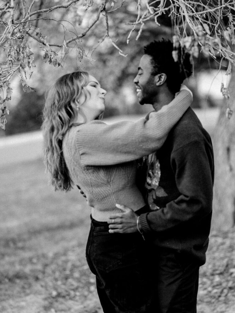 A couple dances under a tree, with their arms wrapped around each other. They are smiling at each other.