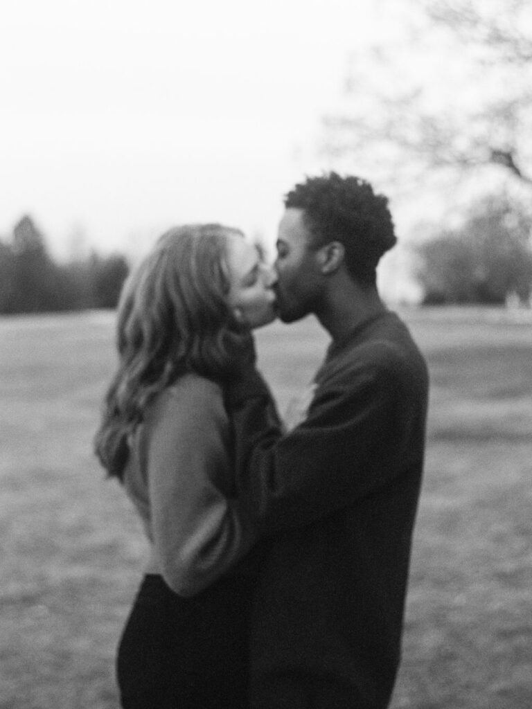 A black and white photograph of a couple kissing in an open field of a park in downtown Denver.