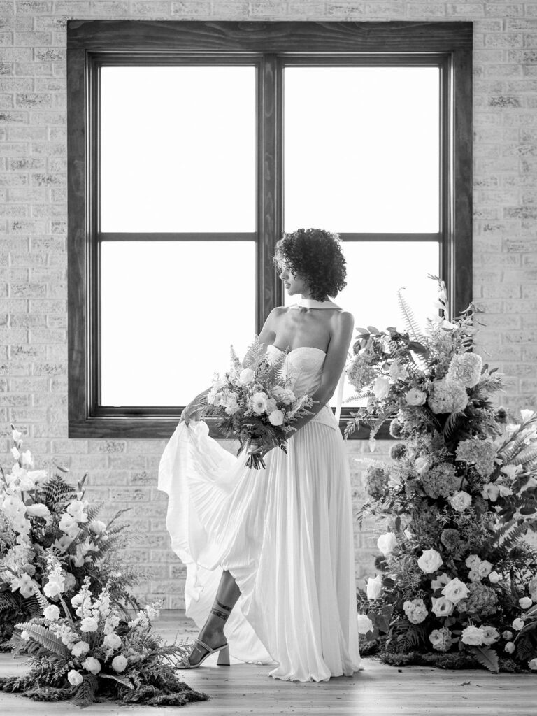 A bride in a drop waist wedding gown stands among a floral installation at a Colorado wedding venue.