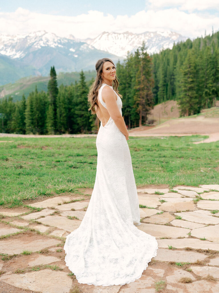 A bride in a low back lace gown with a long train turns over her shoulder in a wedding portrait in Vail, Colorado.