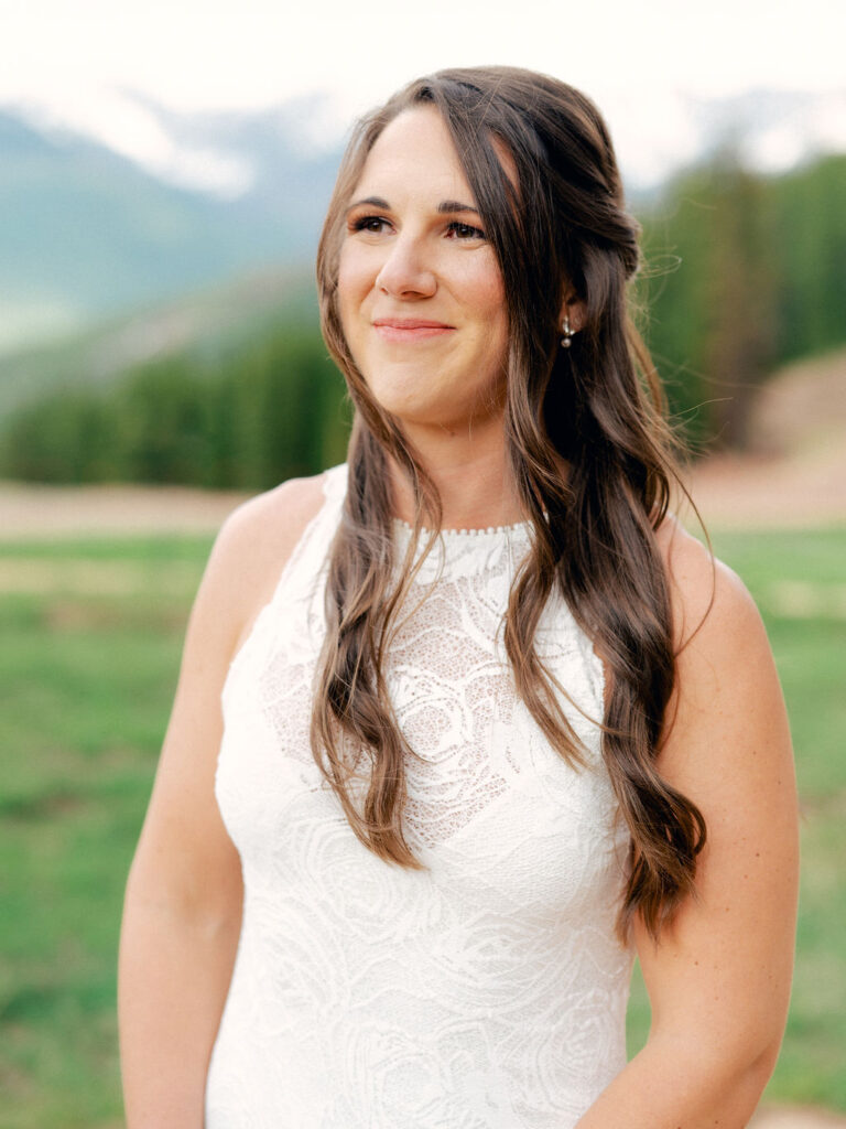 A bride in a high neck lace gown looks off at her husband during their wedding portraits in Vail, Colorado.