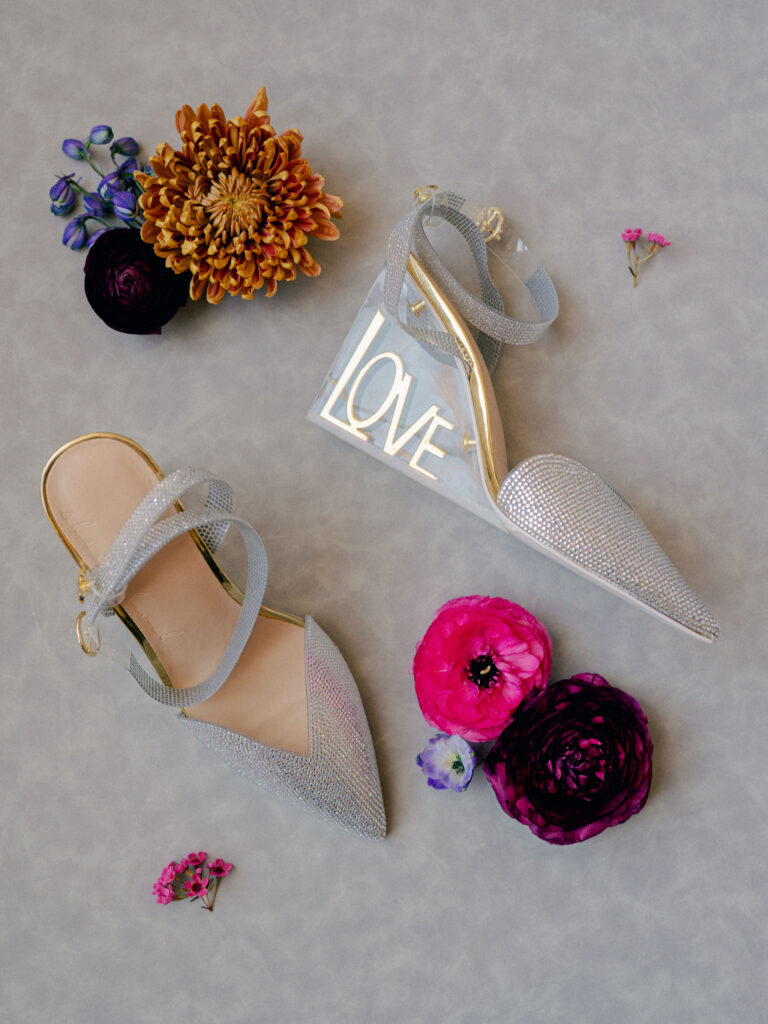 A detail flatlay of a bride's sparkly wedding shoes with an acrylic heel with the word "Love" inscribed in it.