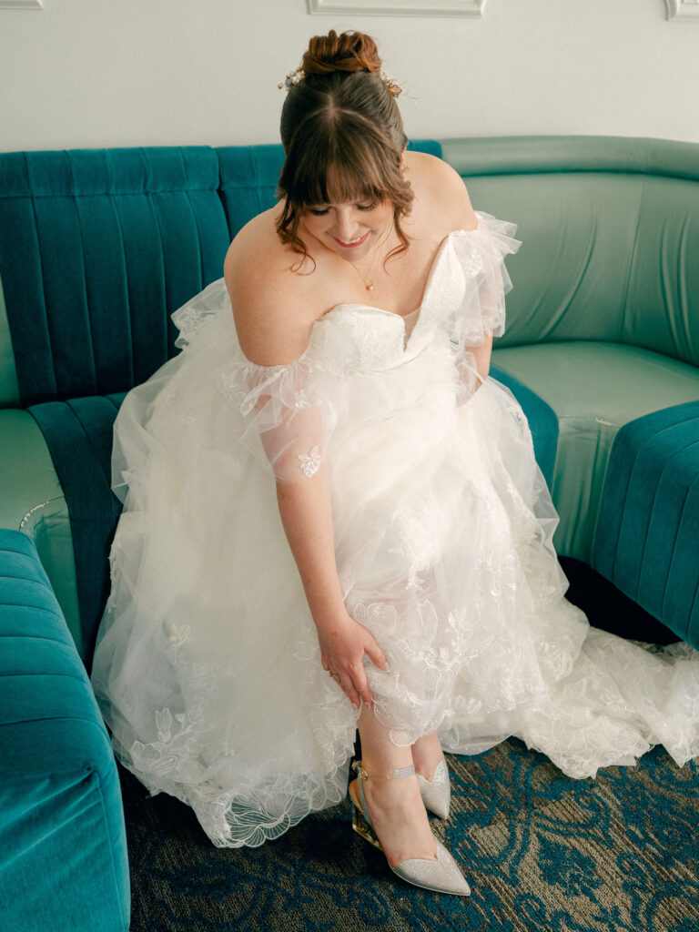 A bride puts on her shoes in a lace wedding gown at her colorful Oklahoma City wedding.