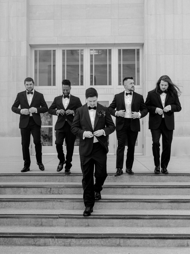 A groom and his groomsmen walk down the front steps of the Oklahoma City Civic Center.