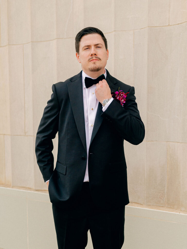 A groom straightens his bow tie in a classic portrait at his Oklahoma City wedding.