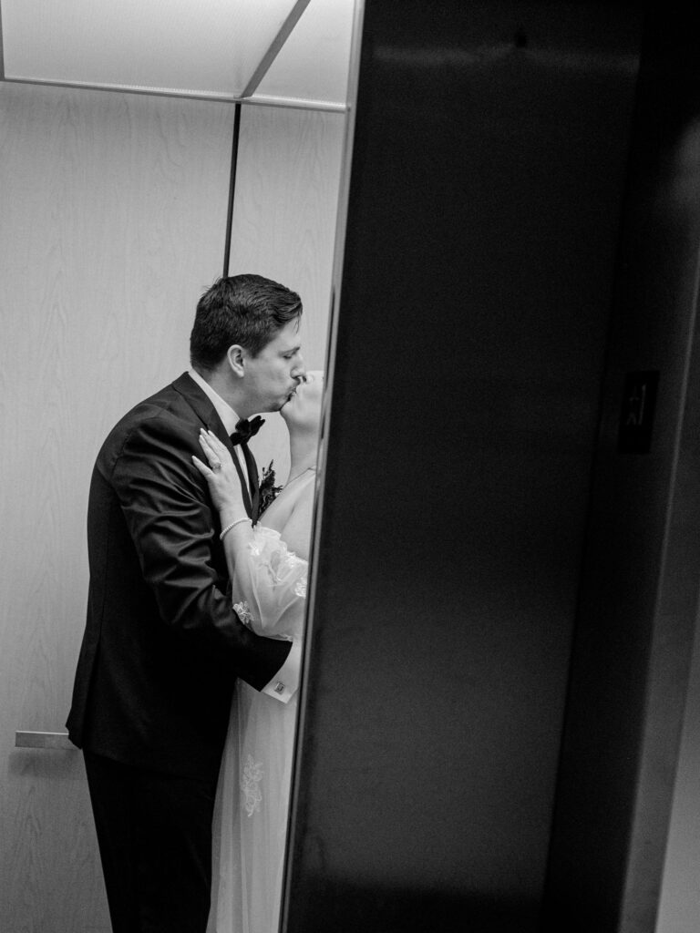 A bride and groom kiss in an elevator as the door is closing.