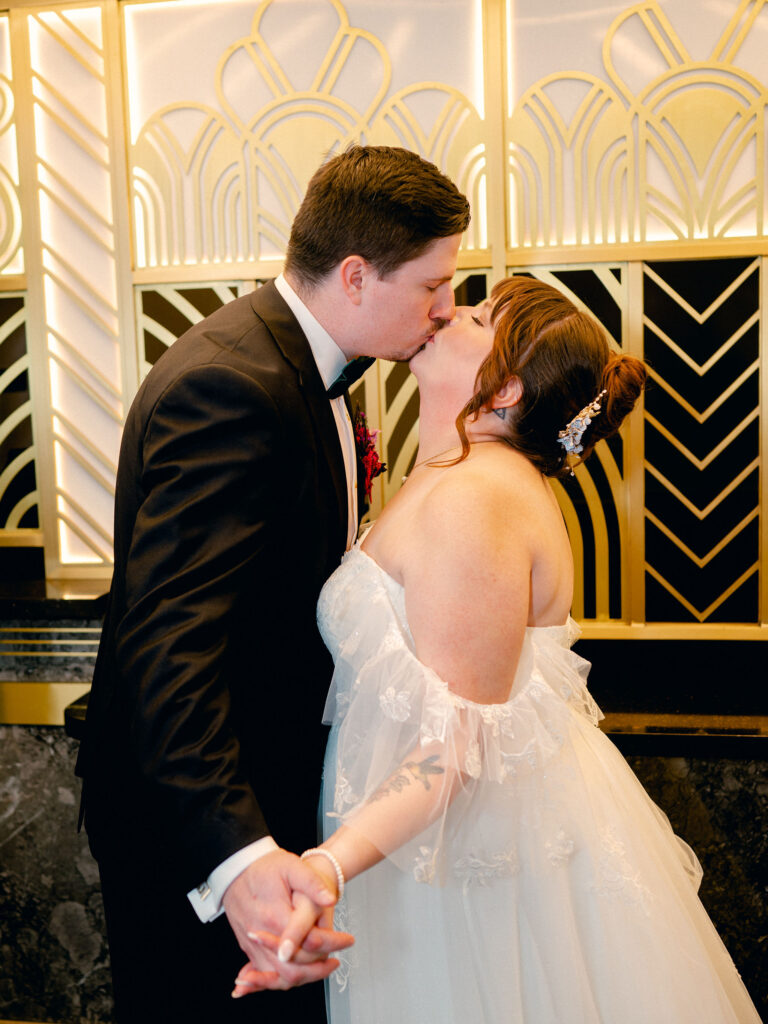 A bride and groom kiss in front of the art deco box office of their Oklahoma City wedding venue.