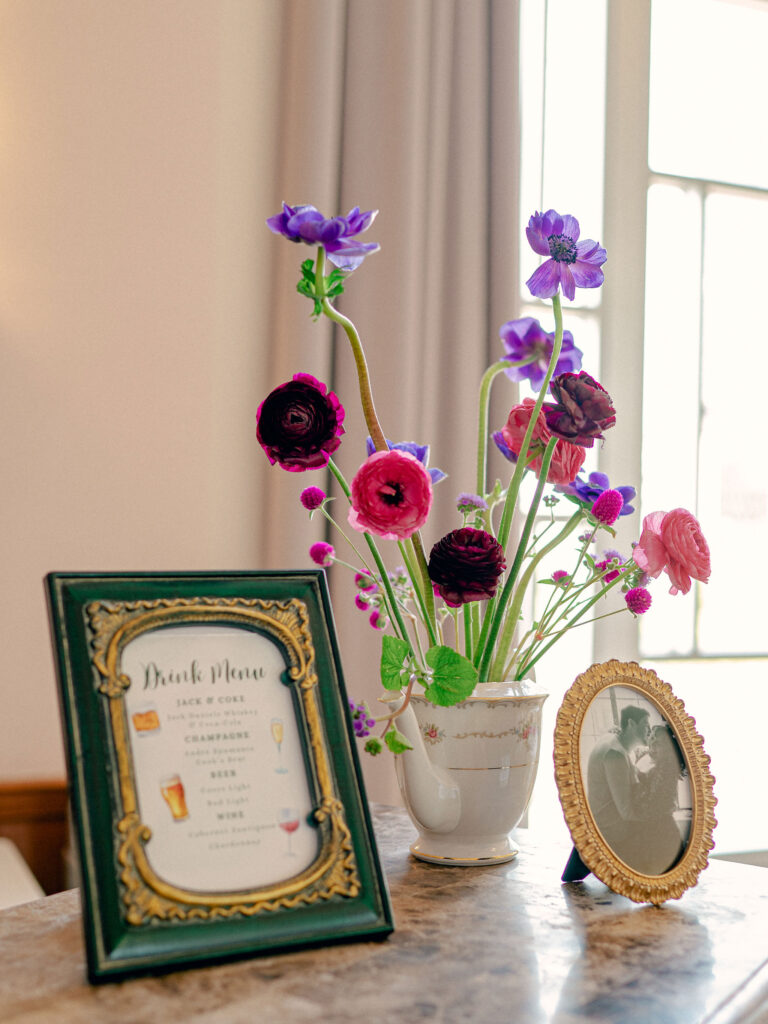 The bar set up at this Oklahoma City wedding included a custom drink menu and an arrangement of jewel tone florals in an antique tea pot.